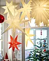 Dekorativa stjärnor hänger framför ett fönster med en julgran i bakgrunden.