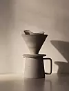 Keramisk kaffebryggare med filter på ett bord mot ljus vägg.