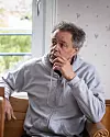 Man i grå hoodie sitter i en kökssoffa vid ett fönster och håller handen mot hakan.