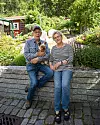 Ett äldre par sitter på en stenmur i en grön trädgård med en liten hund i knät.