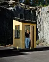 En liten gul byggnad vid en klippvägg med en person i dörröppningen.