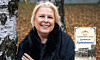En leende kvinna står vid en björk i en park med höstlöv och håller armarna korsade.