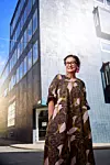 Kvinna i mönstrad klänning står framför en hög modern byggnad med många fönster.