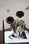 Blommor i en glänsande metallvas står på en bok på ett bord.