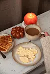 Kaffe, våfflor, kakor och ett tänd pumpaljus på ett rustikt bord.