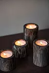 Fyra tända ljus i mörka cylindriska hållare på ett träbord.