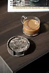 Kopp kaffe och rund dekorationsdetalj på mörkt träbord med en bok i bakgrunden.