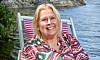 Ruth Kvarnström-Jones sitter i en randig stol vid vattnet och ler mot kameran.