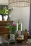 Dukat bord med tekanna, ljusstakar, glas och blomsterarrangemang i ett ljust rum.