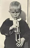 Svartvitt foto av ett litet barn som håller och blåser i en trumpet.