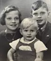 Svartvitt foto av tre barn som poserar tätt tillsammans i ett klassiskt familjeporträtt.