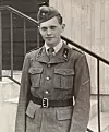 Svartvitt foto av en ung man i militäruniform framför en trappa och en byggnadsfasad.