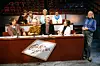 Paneldeltagare och programledare sitter vid ett bord i en tv-studio med tomma publikrader bakom.