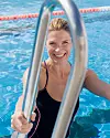 Leende kvinna i poolen håller i en metallstege.