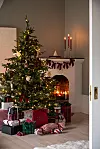 Julsmyckad gran med paket framför en öppen spis med levande ljus.