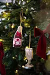 Närbild av en julgran med ljus, röda rosetter och två ornament som liknar en flaska och ett glas.