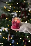 En hand håller ett rött ljus märkt ”GOD JUL” framför en julgran.