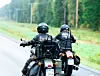 Två motorcyklister kör på en asfalterad väg genom ett skogsområde.