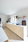 Ljust modernt kök med beige skåp, öppna hyllor och fönster i bakgrunden.