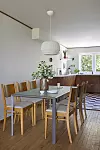 Matrum med fyra trästolar, glasbord, vas med blommor och kök i bakgrunden.