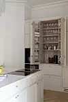 Ljust kök med marmorerad köksö och öppet skåp med glas och burkar.