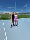 Rikke Holm-Nielsen og Bettina Møller står på en lys blå sportsbane foran et hegn og en grøn fodboldbane.