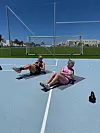 To personer sidder på måtter på en bane og laver maveøvelse med kettlebell.