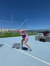 Kvinde i sportstøj laver kettlebelløvelse på lys blå udendørs sportsbane.