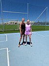 Rikke Holm-Nielsen og Bettina Møller i sportstøj står på en blå udendørs bane foran et hegn i solskin.