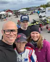 Fyra personer tar en selfie vid en kartingbana med gokartar och tält i bakgrunden.