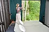 En kvinna står vid ett stort fönster i ett sovrum med utsikt mot skog.