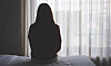 Silhuett av en person som sitter på en säng framför ett solbelyst fönster.