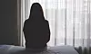 Silhuett av en person som sitter på en säng framför ett solbelyst fönster.
