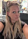 En kvinna tar en selfie inomhus med krukväxter, fönster och möbler i bakgrunden.