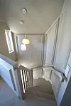 Trappeoppgang med hvite vegger, tretrapp og to hengende lamper.
