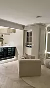 Lyst moderne rom med kjøkken, sofa, lys parkett og dempet belysning. Screenshot.