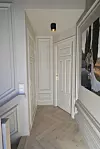 Smal gang med hvite dører, paneler, fiskebeinsgulv og et bilde på høyre vegg.