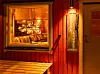 Röd träfasad med upplyst fönster, skylt för bastu och lounge och en bänk utanför.