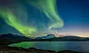 Grönt norrsken lyser över fjäll och vatten i ett mörkt landskap under natthimlen.