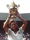En tennisspelare i vit matchtröja håller en stor gyllene pokal över huvudet.