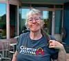 En kvinna med glasögon bär en mörk T-shirt med Cajun Crawfish Festival-motiv utomhus.