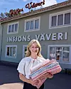 Kvinna håller flera vikta textilier framför fasaden till Insjöns Väveri.