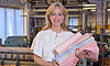Leende kvinna håller flera färgglada textilrullar i en textilfabrik.