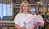 Leende kvinna håller flera färgglada textilrullar i en textilfabrik.