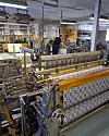 Arbetare vid vävstolar i en fabrik med många textilmaskiner och industriell utrustning.