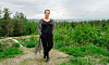 En person står på en grusig stig med grön skog och molnig himmel bakom sig.