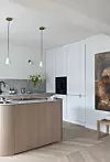 Modernt kök med köksö i trä, vita skåp, hängande lampor och ljusa väggar.