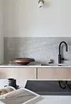 Minimalistiskt kök med ljus träbänk, stenliknande väggskiva, svart kran och dekorativ skål.