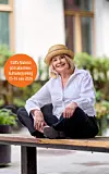 Kvinna i vit skjorta och stråhatt sitter på en bänk utomhus med en orange informationsskylt bredvid sig.