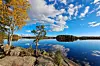 Höstträd vid en klippa ovanför en stilla sjö med öar och blå himmel med moln.